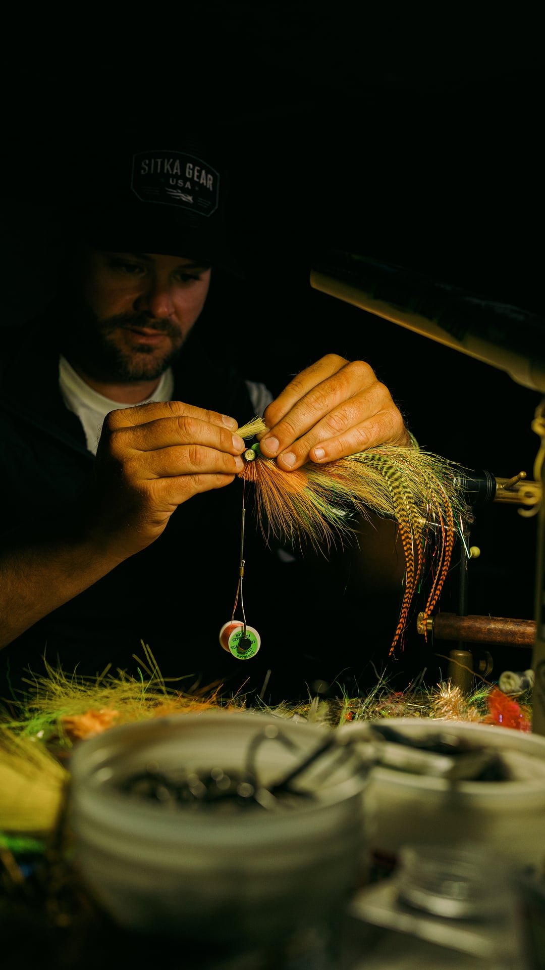 A man inspecting his fishing fly under dim warm light.